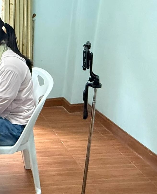 A candidate seated at a desk with a smartphone on a tripod behind her, used as the second camera for the CSCA home-based exam